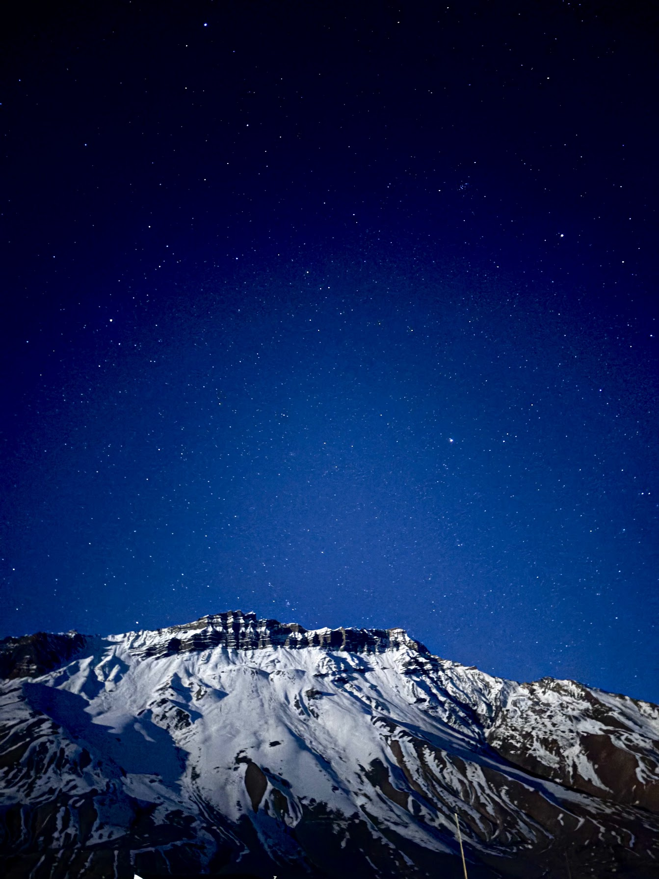 A star-filled blue night sky above snow-covered mountains in Kaza, Himachal Pradesh